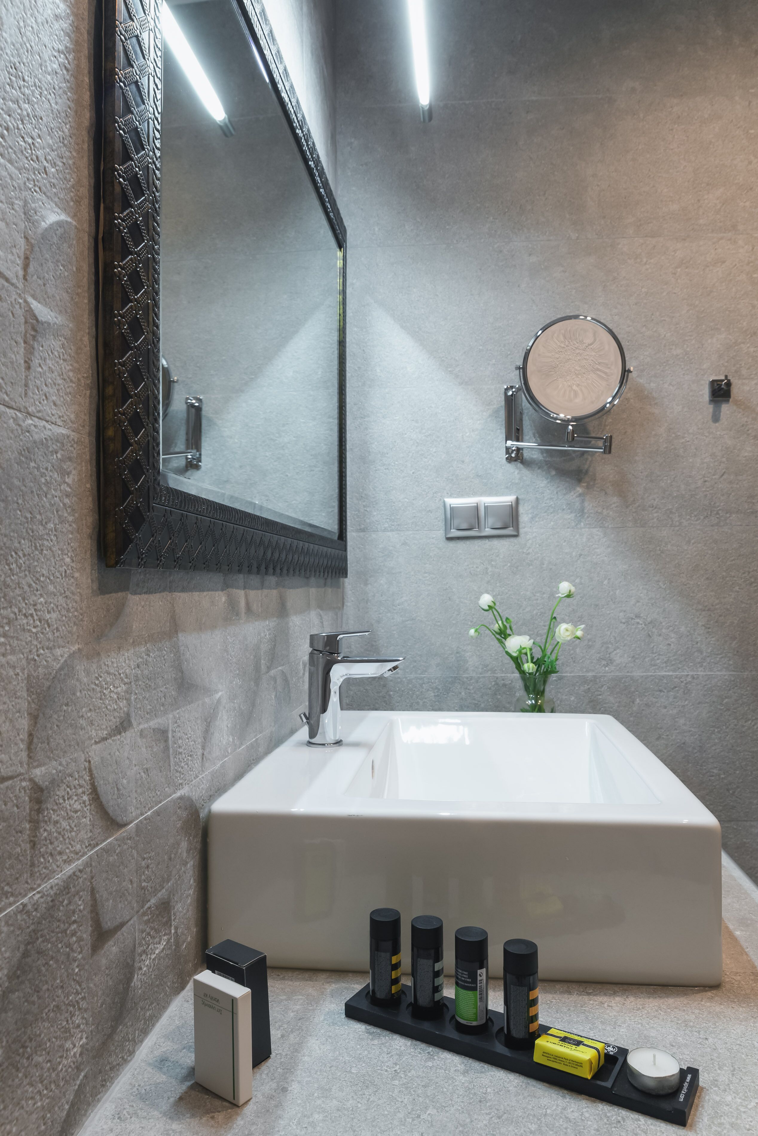A modern bathroom with a large sink, a mirror, a towel rack, and a small vase with flowers.
