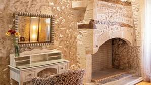 A stone wall with a mirror, a vanity with a glass top, and a patterned cushion. - Avli Lounge Apartments (Rethymno)
