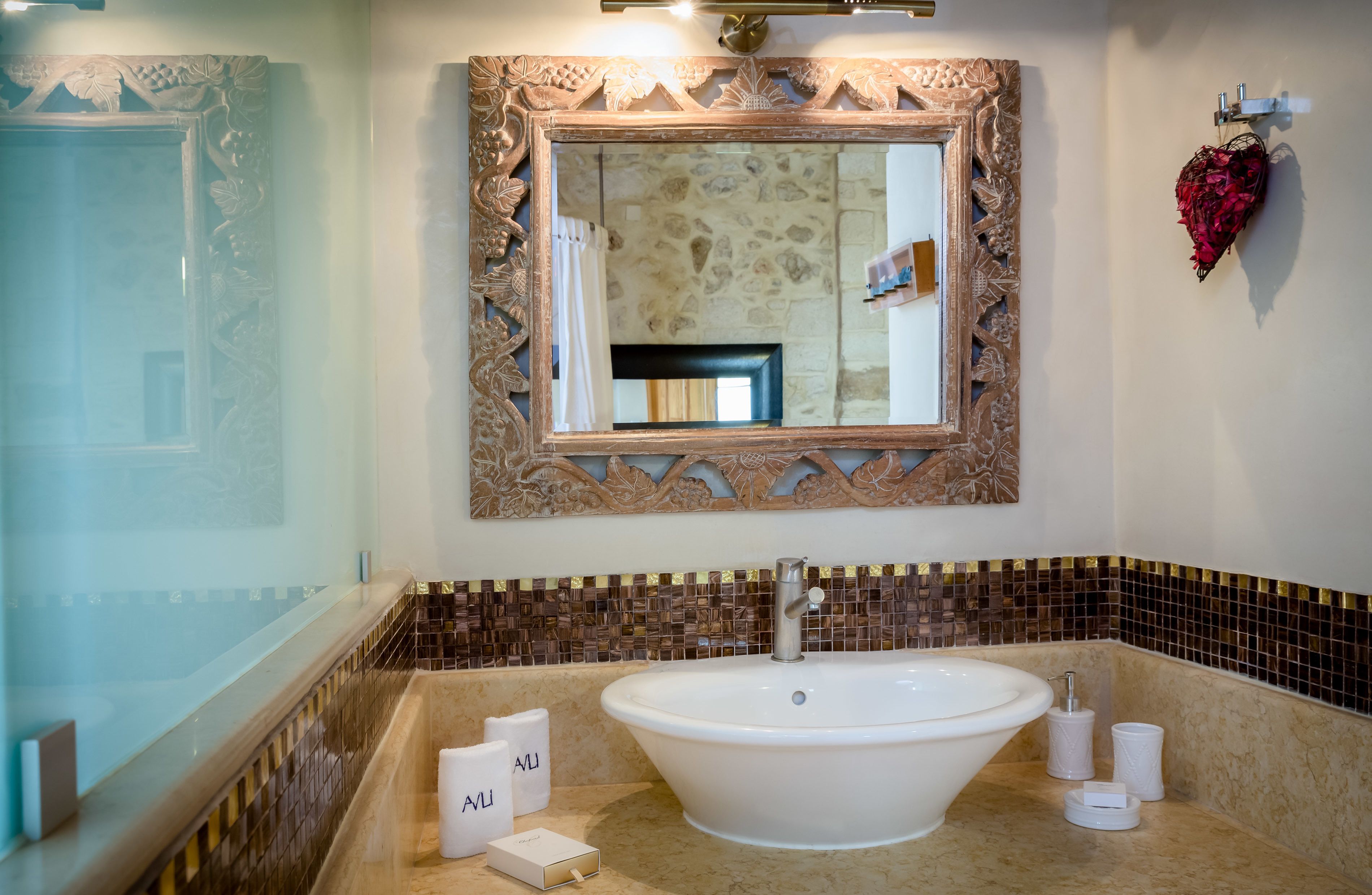 A bathroom with a large oval sink, a mirror with an ornate frame, and a shower area with a decorative wall.
