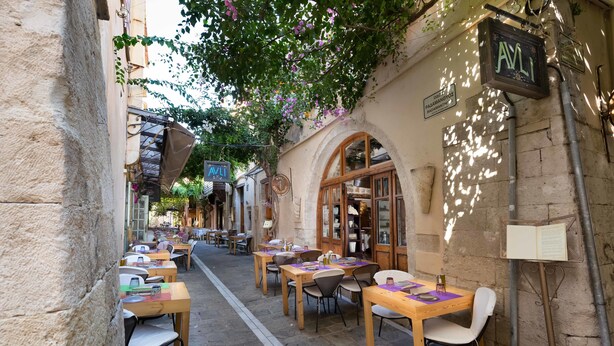 A narrow street with outdoor seating and a building with a sign reading "AVLI". - Avli Lounge Apartments (Rethymno)