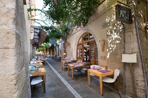 A narrow street with outdoor seating and a building with a sign reading "AVLI". - Avli Lounge Apartments (Rethymno)