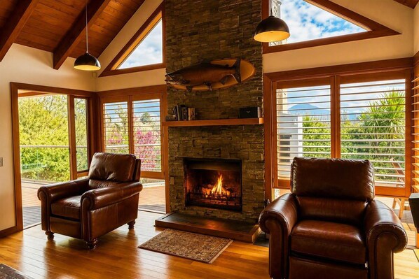 A room with a fireplace, leather chairs, wooden flooring, and large windows with blinds.