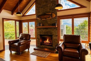 Una habitación con chimenea, sillones de cuero, piso de madera y ventanas amplias con persianas.