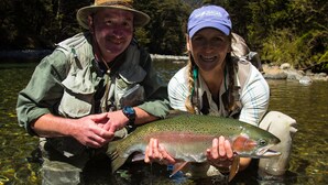 Two people holding a large fish in clear water.