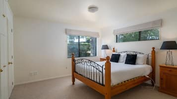 Een slaapkamer met een houten bed, twee nachtkastjes, een raam met uitzicht op groen en een deur.