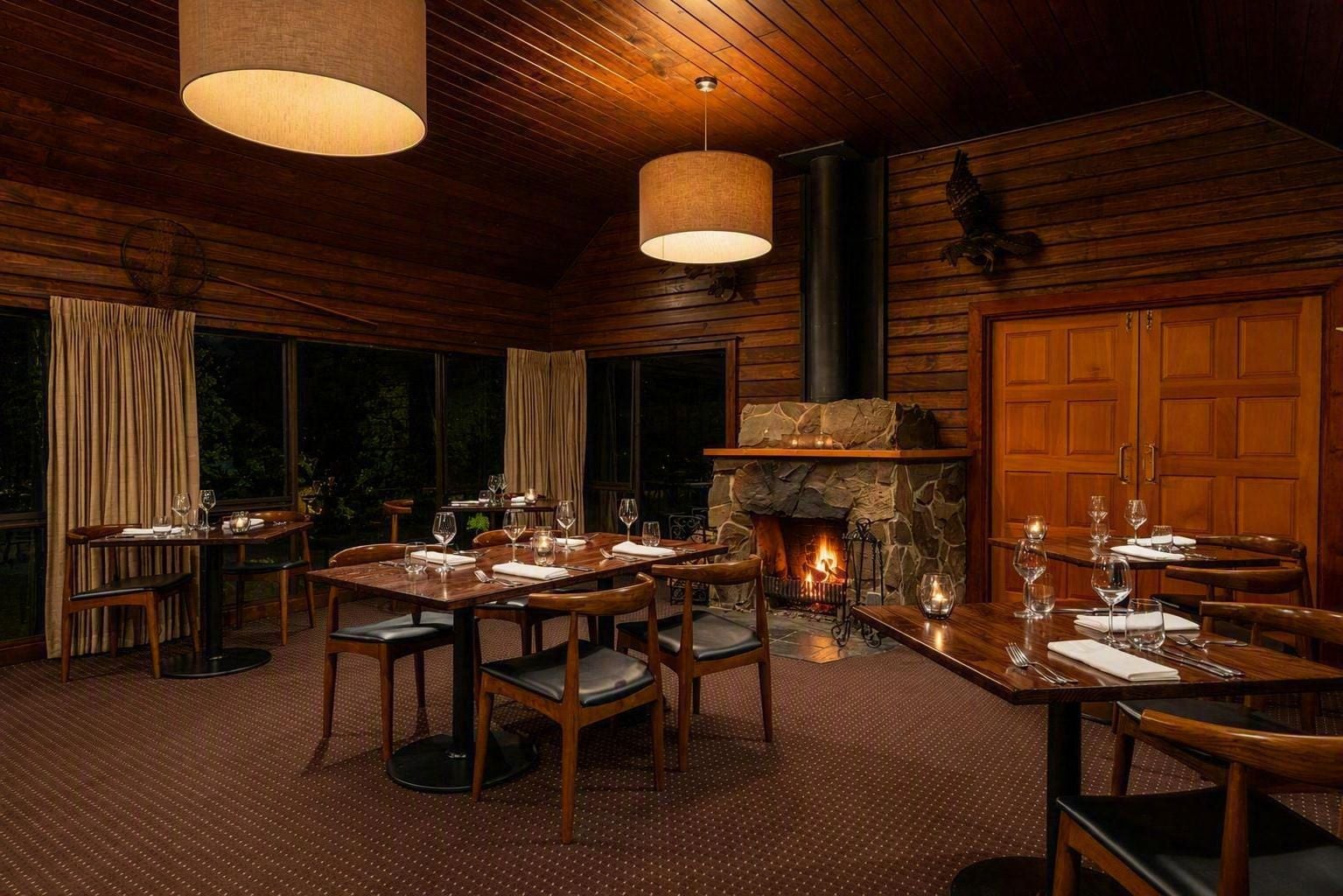 A dining area with a stone fireplace, wooden walls, and large windows.
