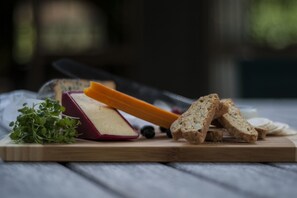 A wooden cutting board with a wedge of cheese, slices of bread, and a small bunch of greens.