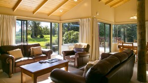 Amplia sala de estar con un gran ventanal, sofás de cuero, una mesa de centro de madera y una zona de comedor con sillas de madera.