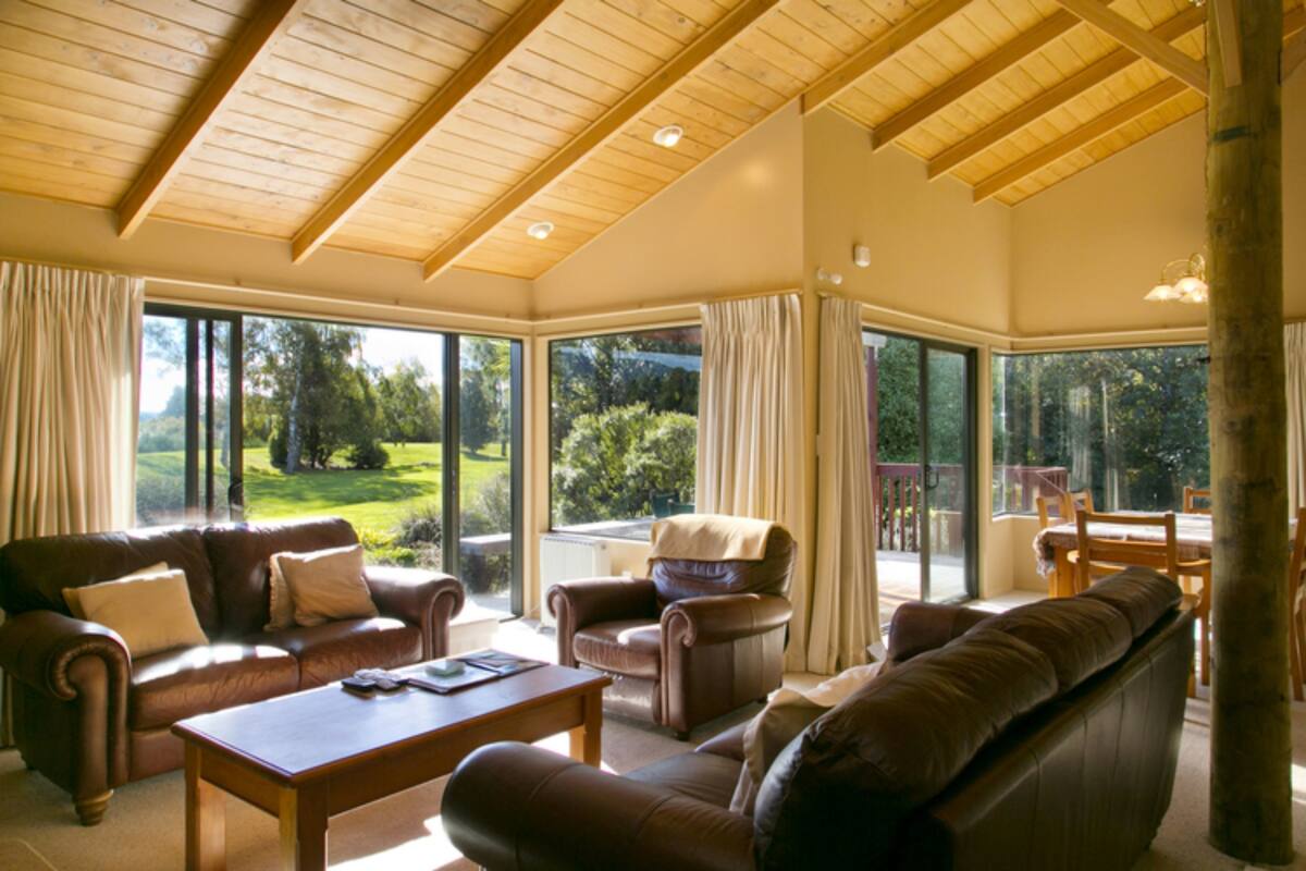 A spacious living room with a large window, leather sofas, a wooden coffee table, and a dining area with wooden chairs.