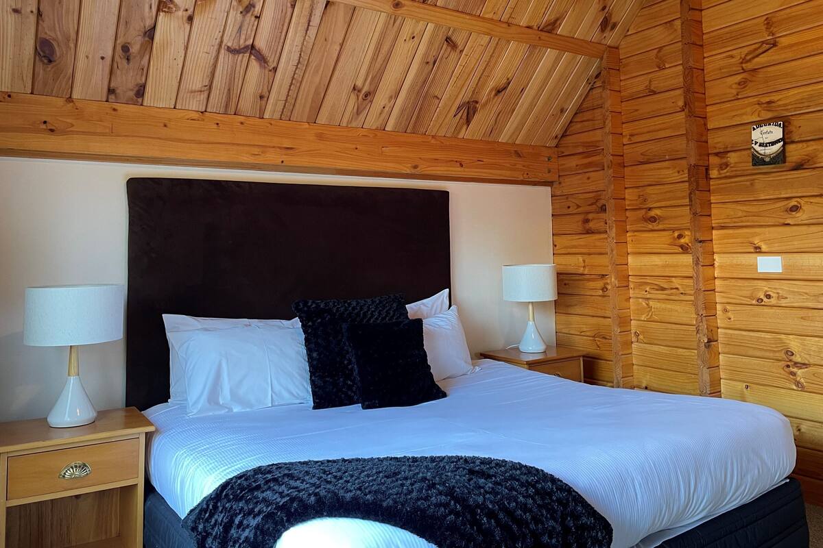 A wooden-paneled room with a large bed, two bedside lamps, and a wall clock.