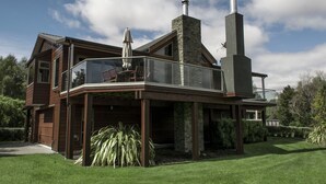 Una casa moderna con balcón de vidrio, chimenea y césped cuidado.