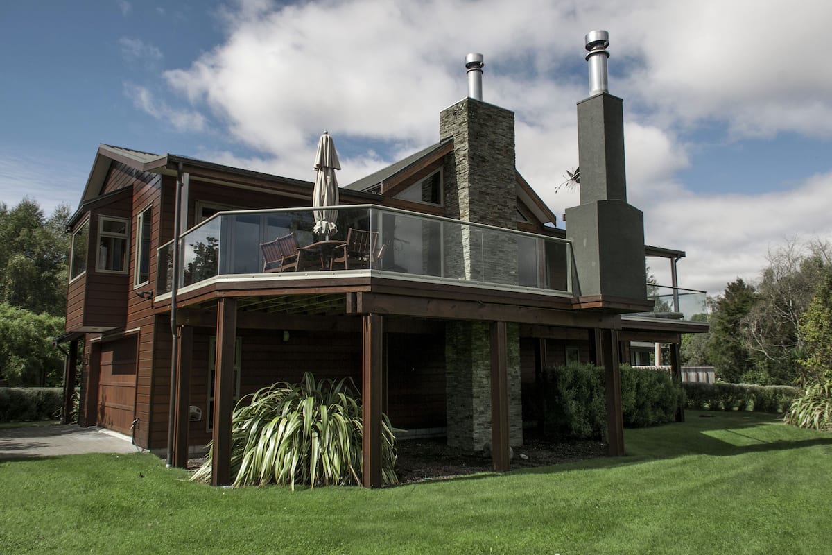 A modern house with a glass balcony, a chimney, and a well-maintained lawn.