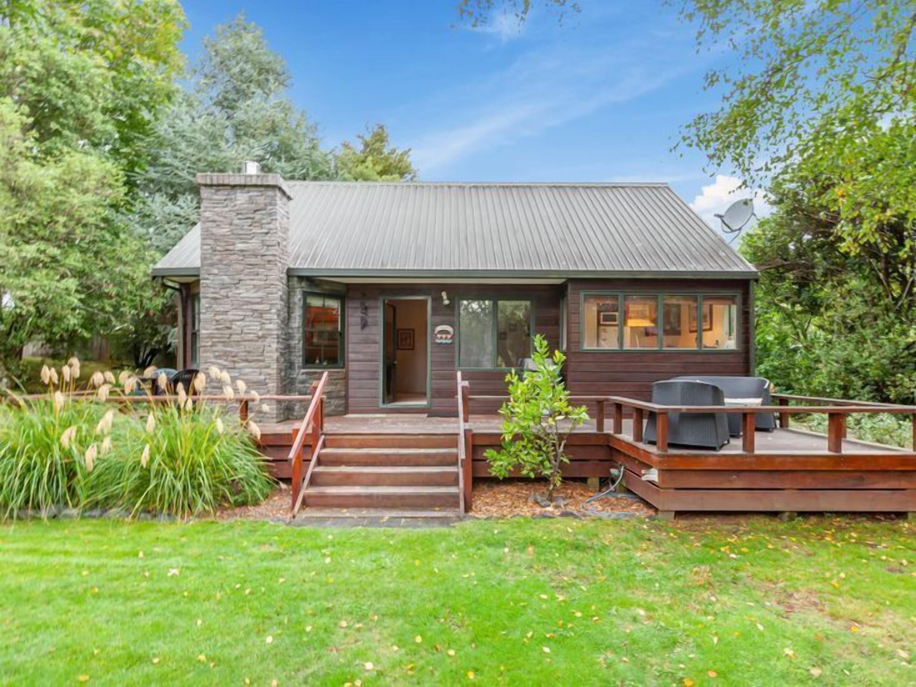 A small, rustic cabin with a stone chimney, wooden deck, and a covered porch.