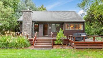A small, rustic cabin with a stone chimney, wooden deck, and a covered porch.