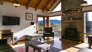 Amplia sala de estar con chimenea, vigas de madera, televisor y vistas a las montañas.