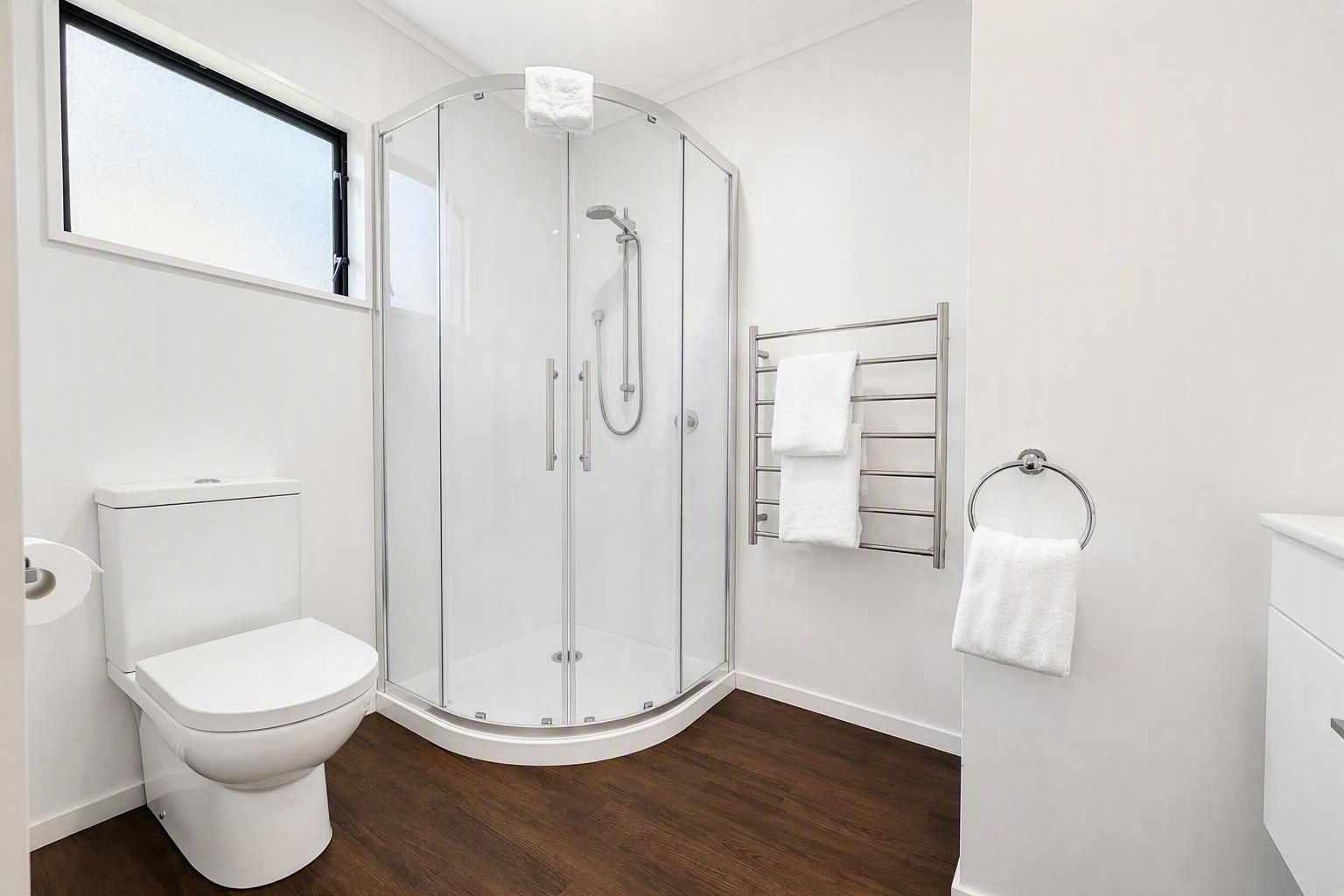 Un baño moderno con ducha de mampara de vidrio, inodoro y perchero para toallas.