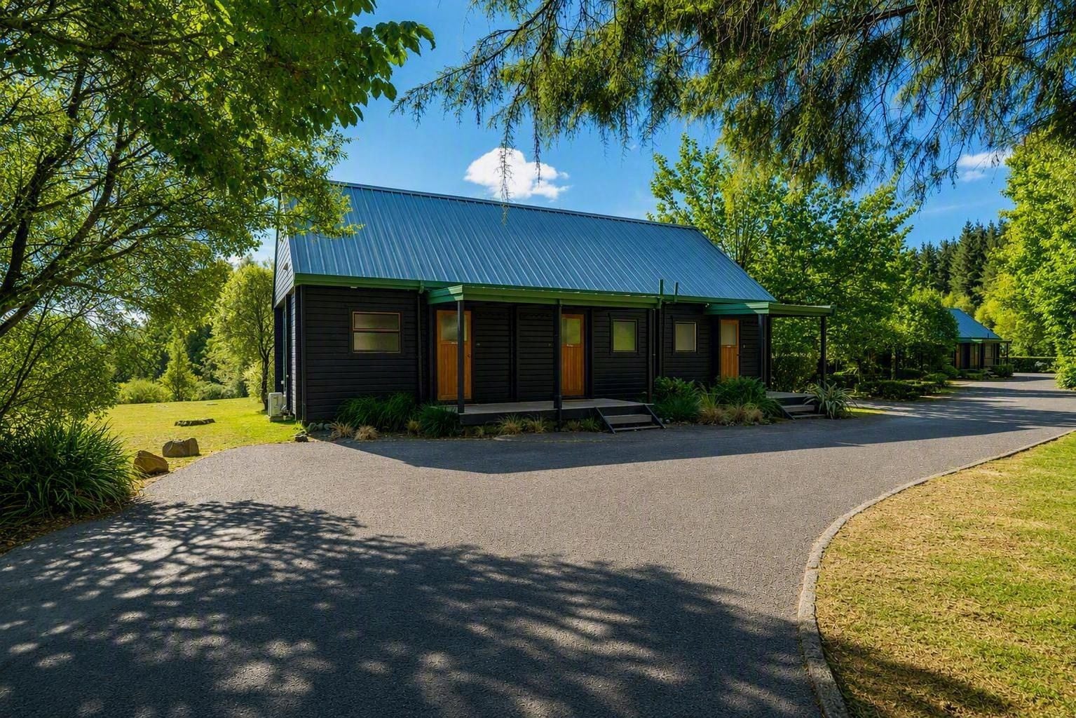 A single-story building with a dark exterior, a green roof, and a paved driveway leading to the entrance.
