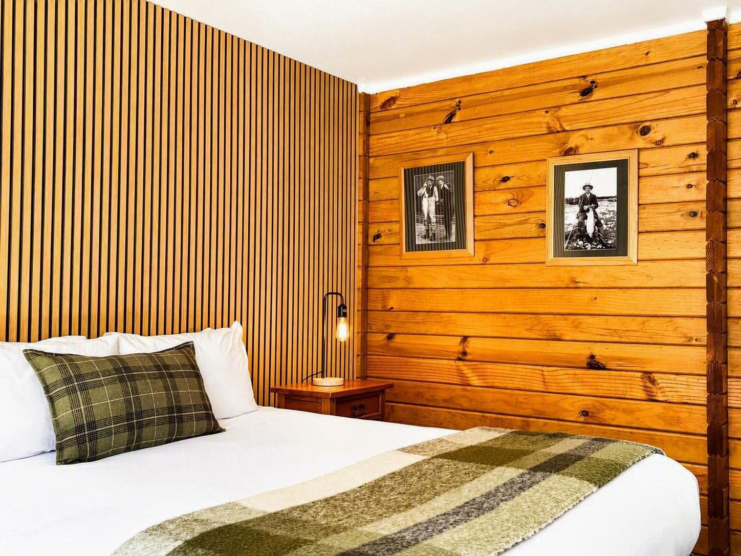 Una habitación con una cama, una mesita de noche, una lámpara y dos cuadros en la pared.
