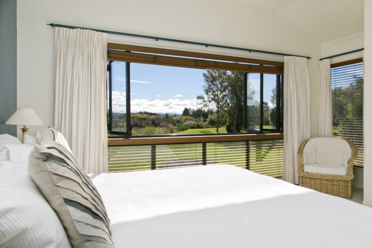 A bedroom with a large window, a bed, a chair, and a lamp.