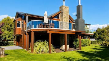 Una casa moderna de dos pisos con un balcón de vidrio, una chimenea de piedra y un césped bien cuidado.