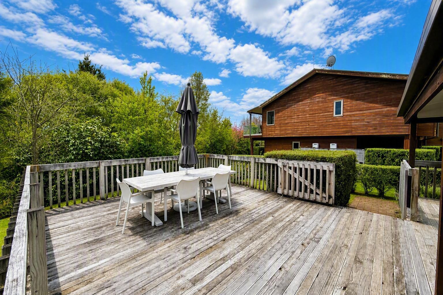 A wooden deck with a table and chairs, surrounded by a wooden fence, and a house in the background.