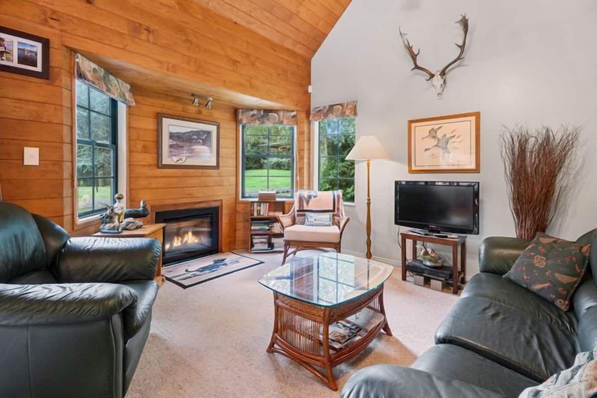 A cozy living room with a fireplace, leather sofas, a glass coffee table, and a mounted deer head.