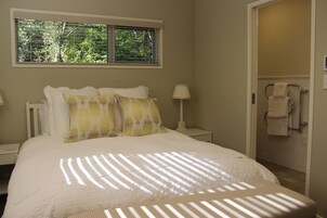 Un dormitorio con cama, mesita de noche, ventana con persianas y baño con toallero.