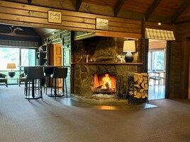 Un interior acogedor con chimenea de piedra, vigas de madera y un comedor con sillas.