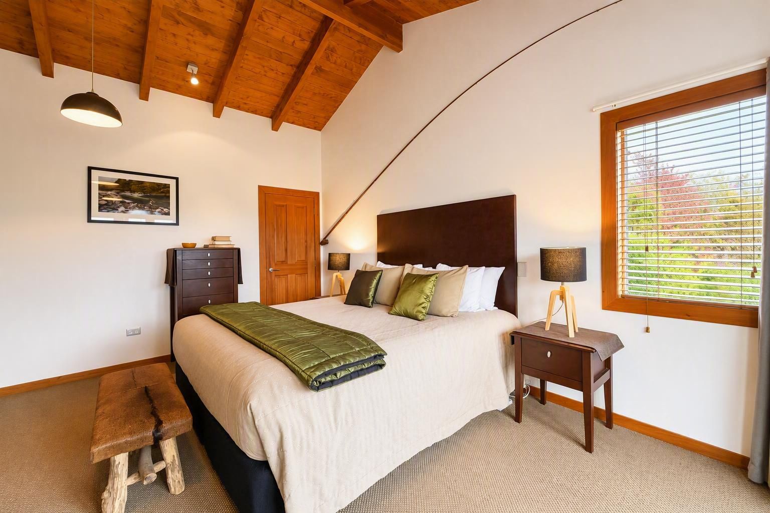 A bedroom with a bed, bedside table, lamp, and a window with blinds.
