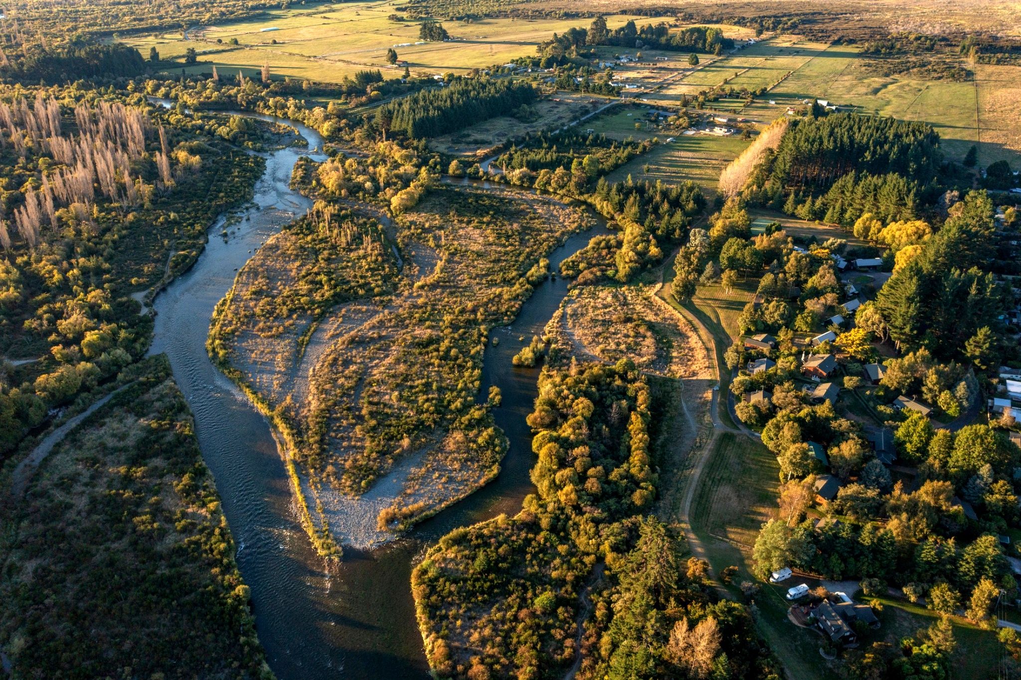 An aerial view of a rural landscape with a river, fields, and scattered houses.