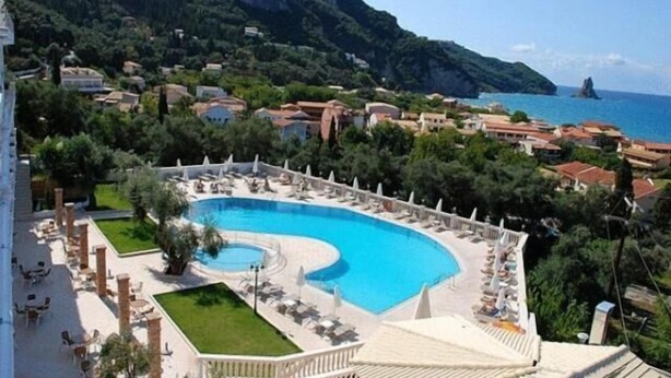 Un resort con una piscina grande rodeada de sillones de descanso y vistas al mar y a las montañas.