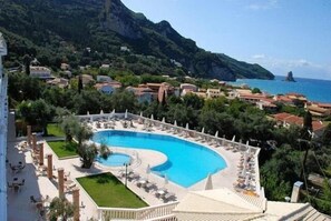 A resort with a large pool surrounded by lounge chairs and a view of the sea and mountains. - Aloha Hotel (Corfu)