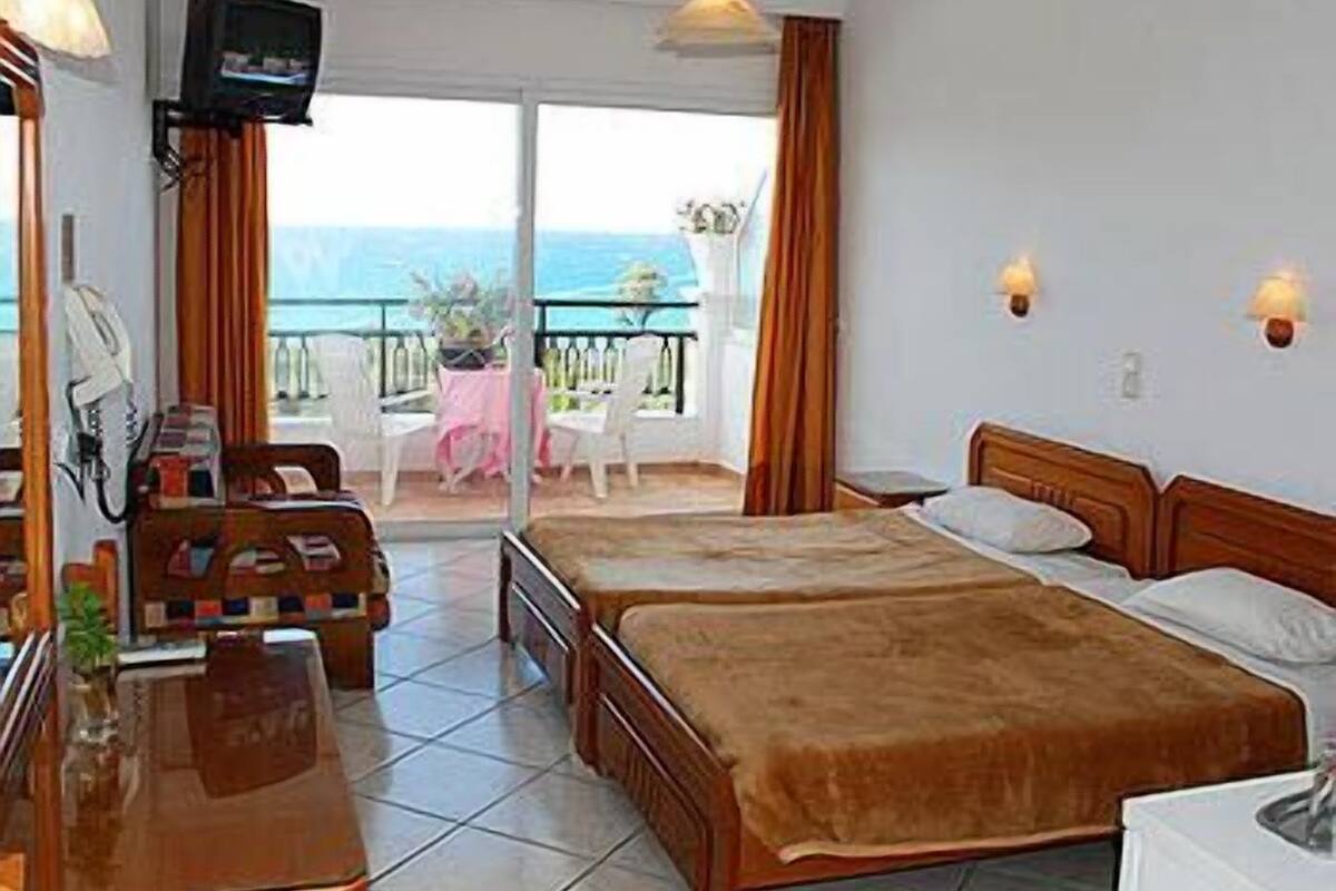 Habitación de hotel con dos camas, un escritorio, televisor y balcón con vista al mar.