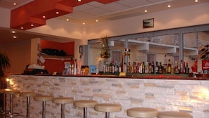 Zona de bar con pared de piedra, varios taburetes y una variedad de botellas en estanterías.