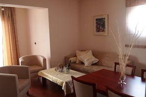 A living room with a sofa, armchairs, a dining table, and a painting on the wall.