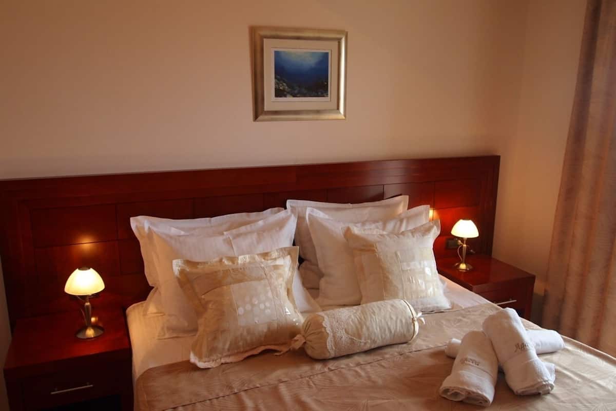 A neatly made bed with white linens, two bedside lamps, and a framed picture on the wall.