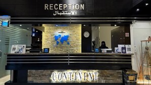 Un área de recepción con suelo de mármol, una mesa de recepción y tres retratos enmarcados.