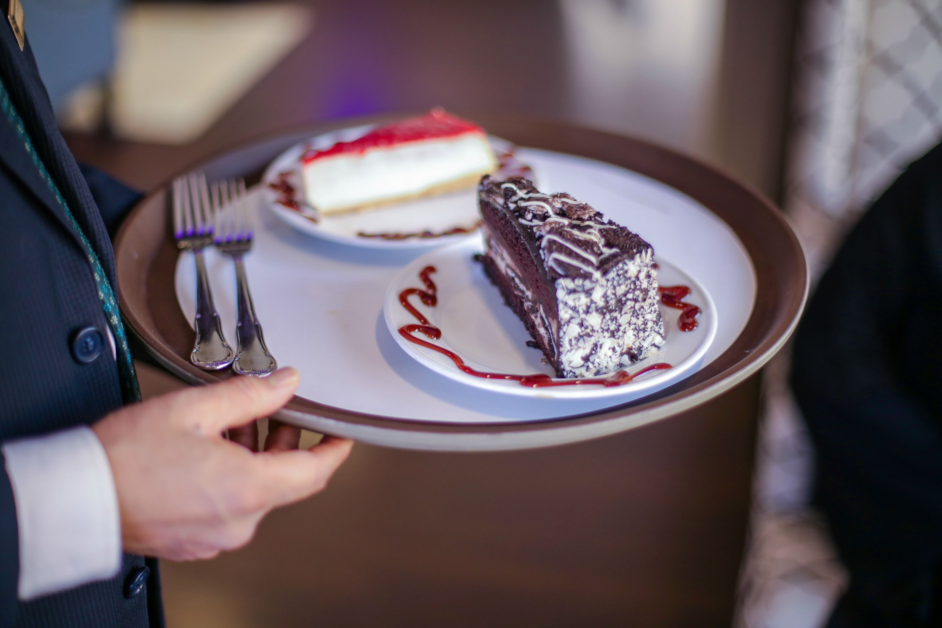 Een persoon houdt een bord vast met twee taartjes, waarvan er één rood beslag heeft en de andere chocolade glazuur.