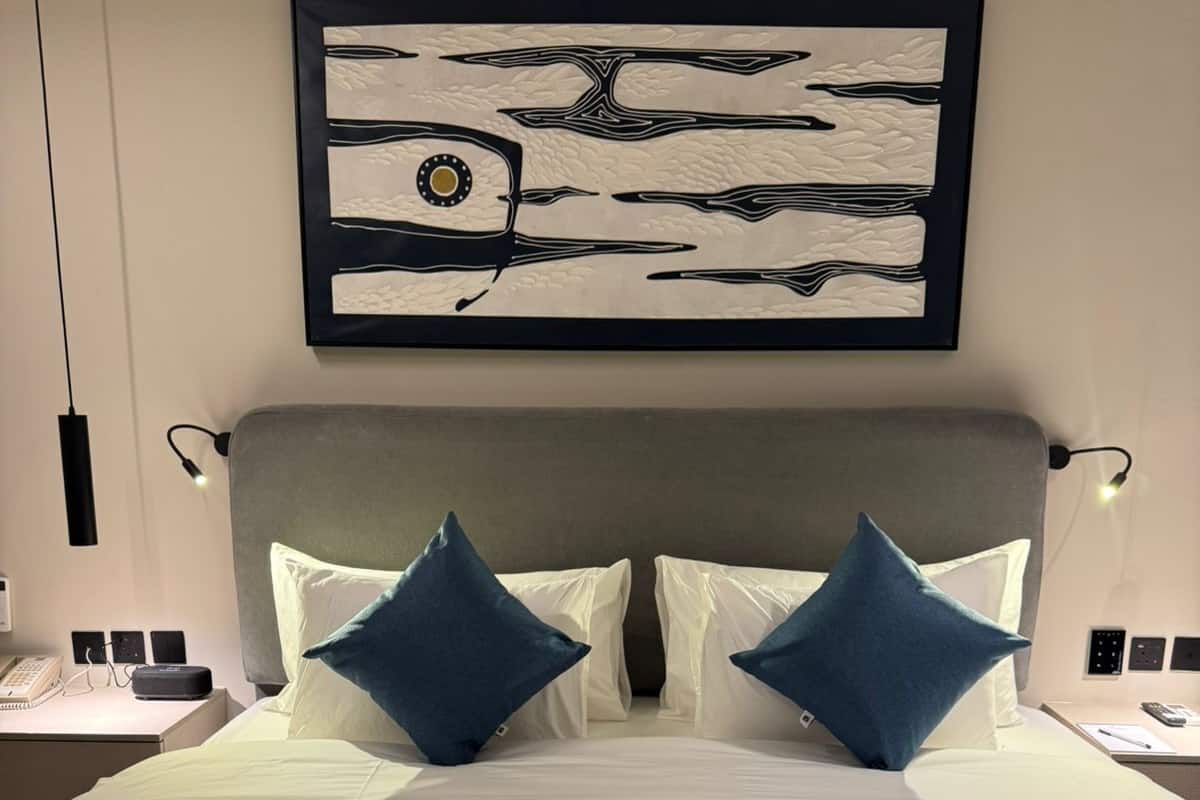 A neatly made bed with a grey headboard, two blue pillows, and a framed artwork above it.