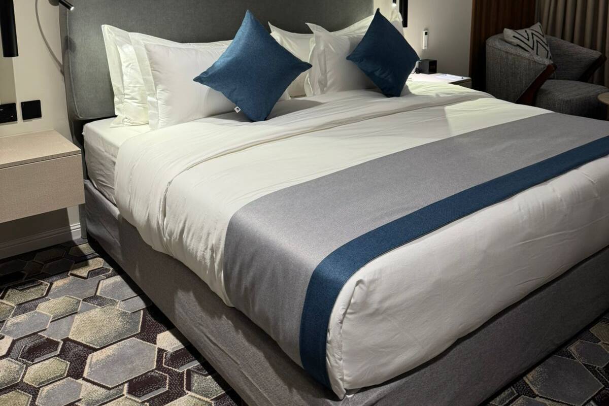A neatly arranged hotel room with a large bed, a bedside table, a wall-mounted artwork, and a patterned carpet.