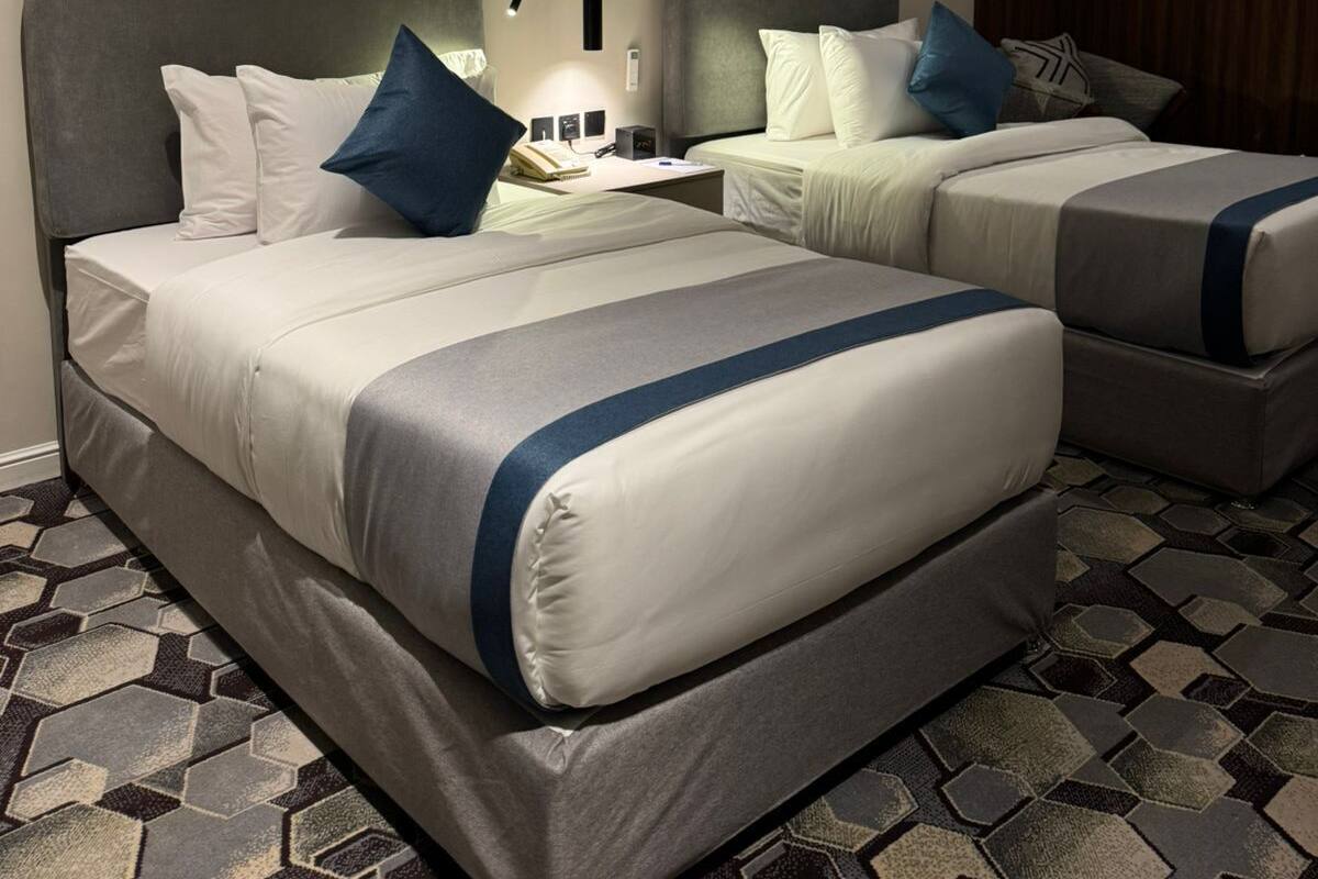 A hotel room with two beds, a large abstract painting on the wall, and a geometric patterned carpet.