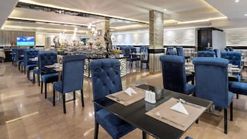 Un restaurante moderno con sillas de respaldo alto, una barra central y una pantalla de televisión.