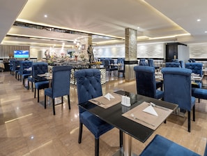 A modern restaurant with high-backed chairs, a central bar area, and a television screen. - LE DIYAR Al Waha Hotel Riyadh (Riyadh)