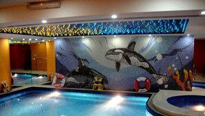 Una piscina interior con un mural de orcas y vida marina, rodeada por un suelo de mosaicos y un techo con luces LED azules.