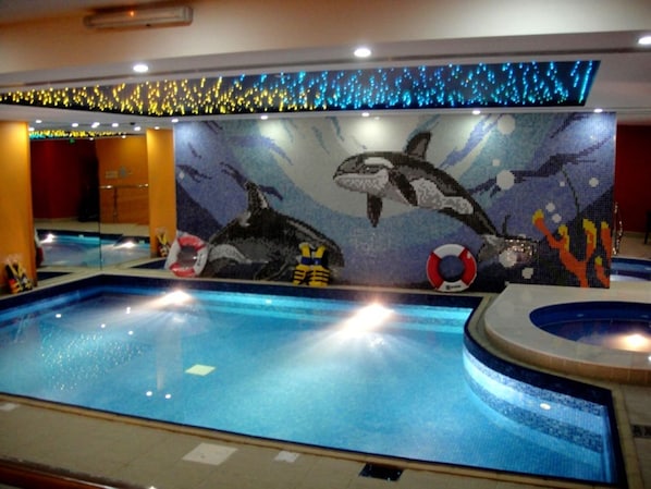 An indoor pool with a mural of orcas and marine life, surrounded by a tiled floor and a ceiling with blue LED lights.