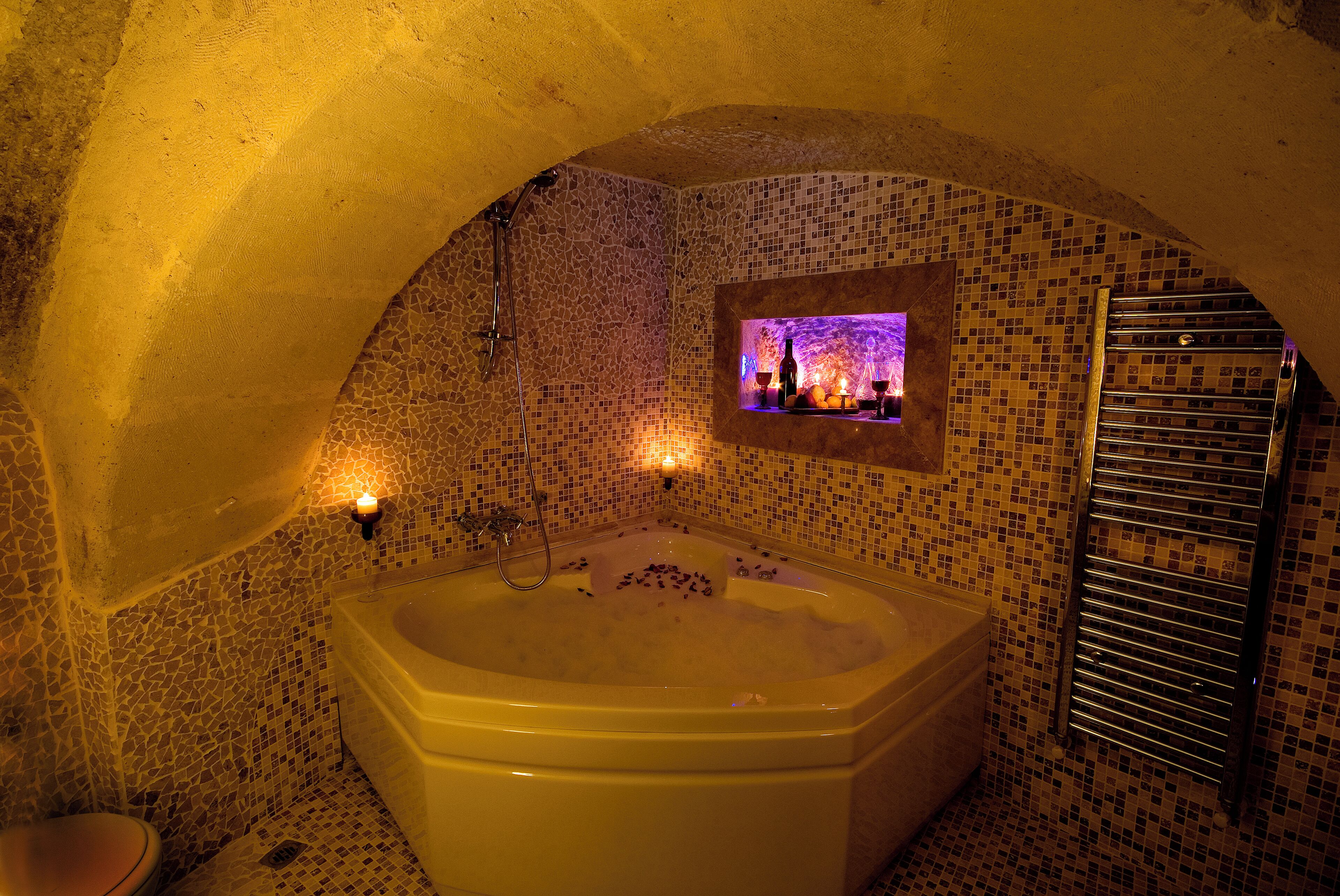A bathroom with a mosaic wall, a bathtub, and a small illuminated display.