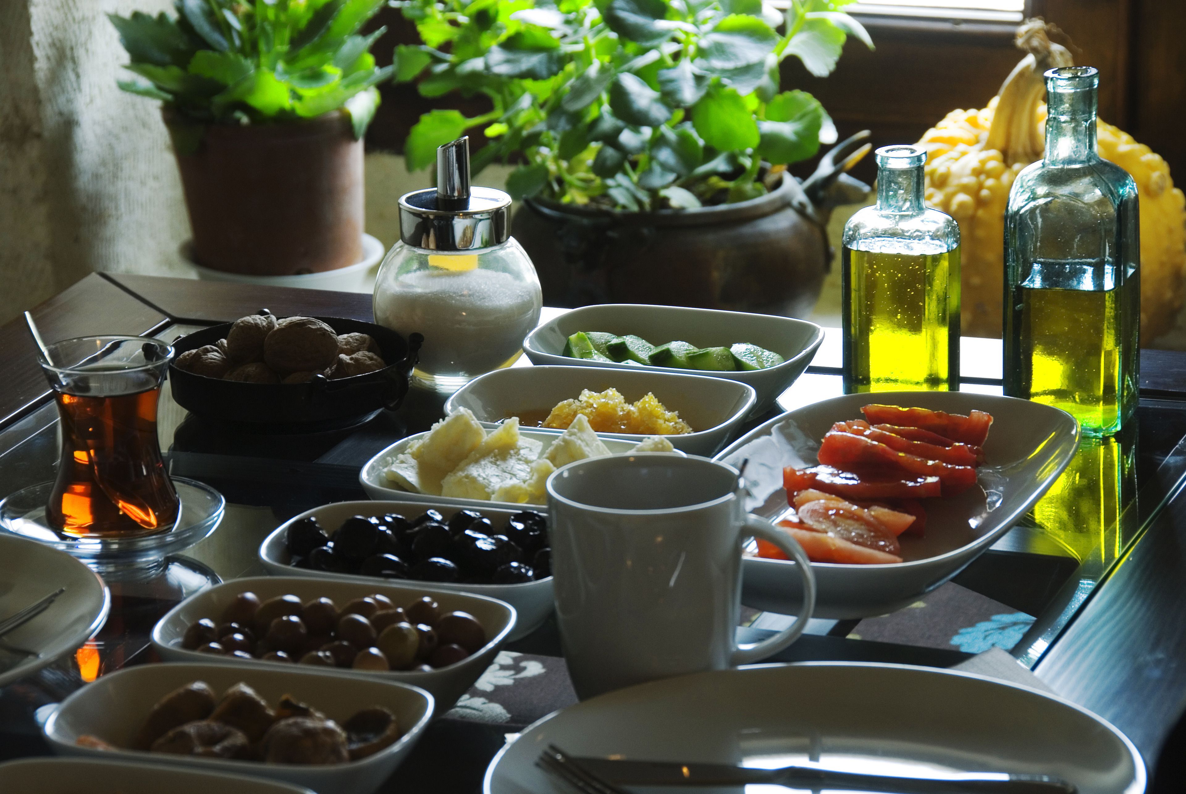Ein Tisch ist reichhaltig mit Speisen gedeckt, darunter Oliven, Tomaten und eine weiße Tasse.