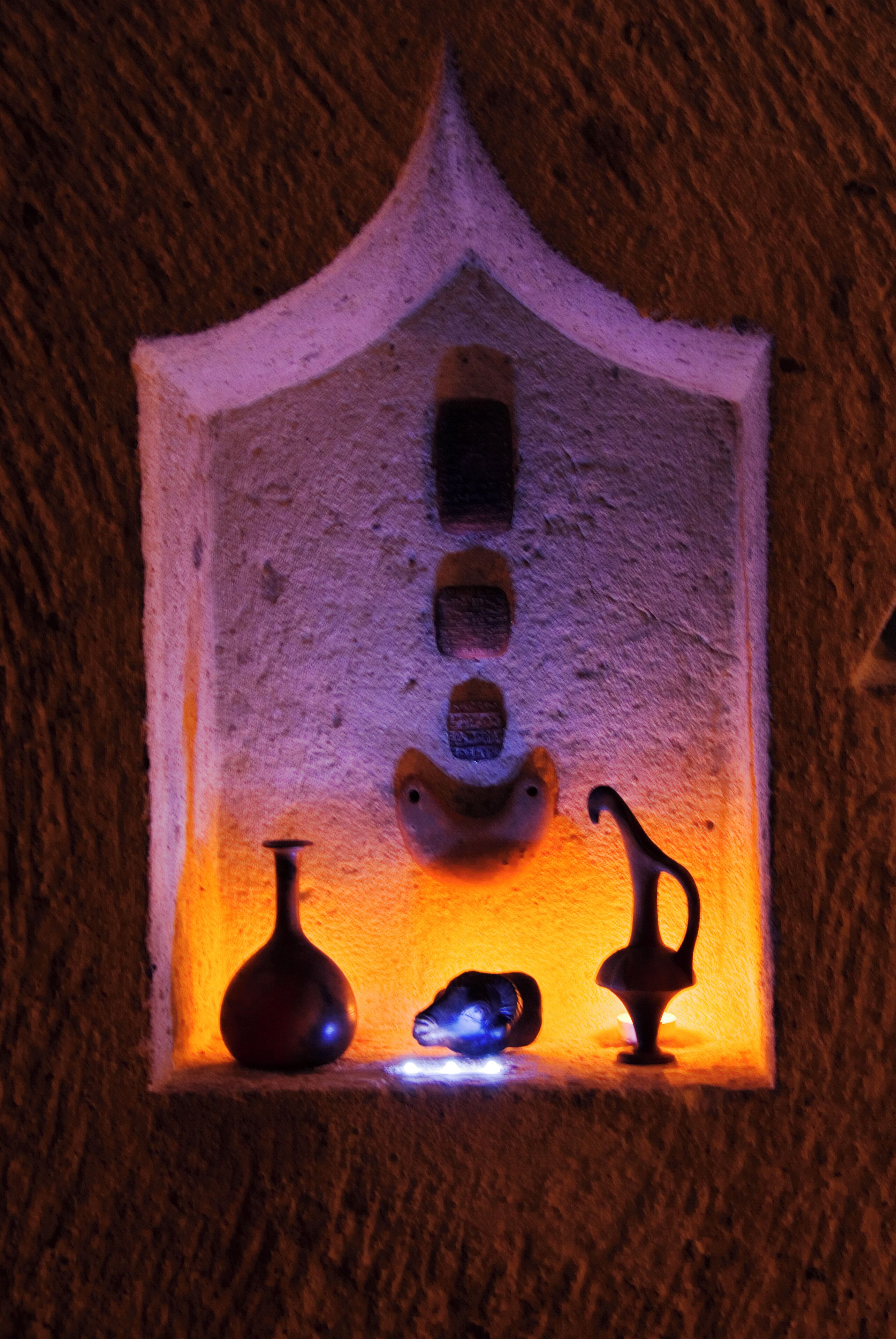 A small, illuminated alcove with a textured wall, a vase, and two figurines.