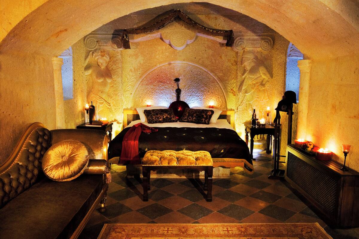 A luxurious bedroom with a checkered floor, a plush sofa, a large bed with ornate headboard, and a fireplace.