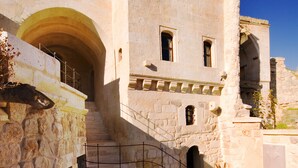A stone building with a staircase leading to an upper level, a potted plant, and a clear blue sky. - Perimasali Cave Hotel - Cappadocia (Ürgüp)